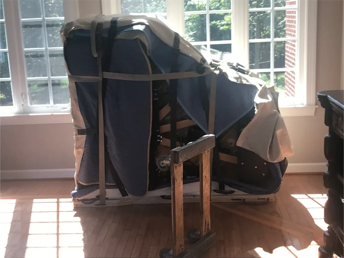 Grand piano wrapped in moving blankets and strapped to a piano board