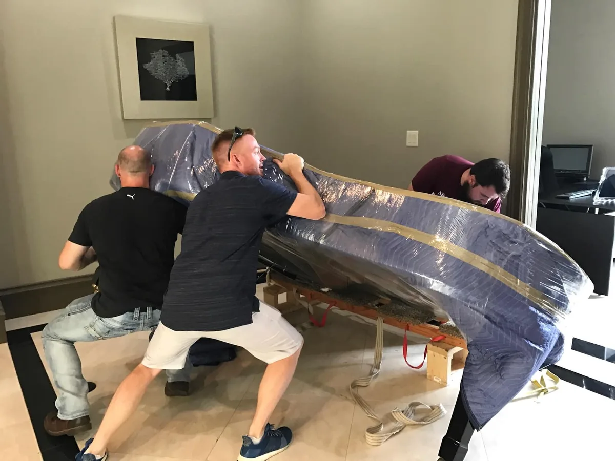 Movers lifting a blanket-wrapped grand piano on its side