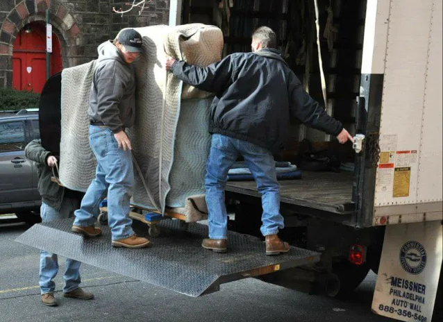 Movers loading a blanket-wrapped piano onto a truck liftgate