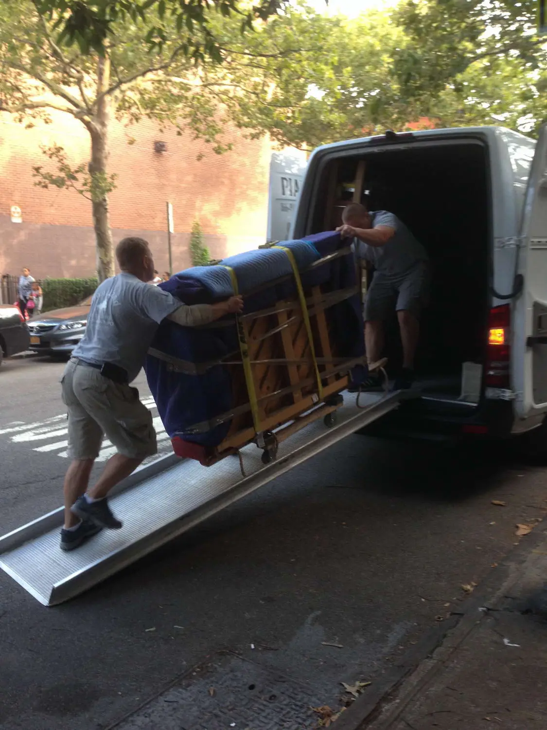 Movers pushing a wrapped piano up a ramp into a van