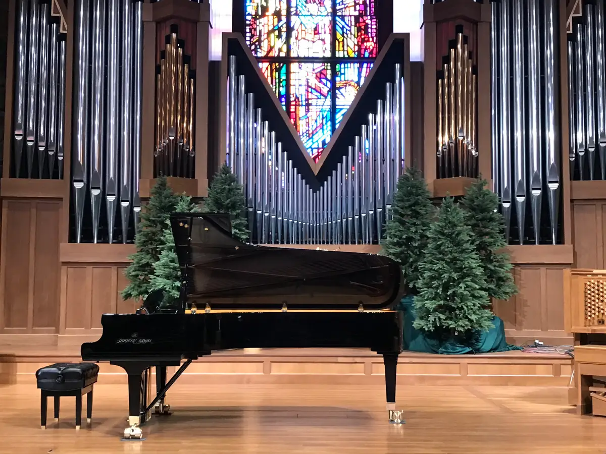 Grand piano on a stage in front of pipe organ pipes