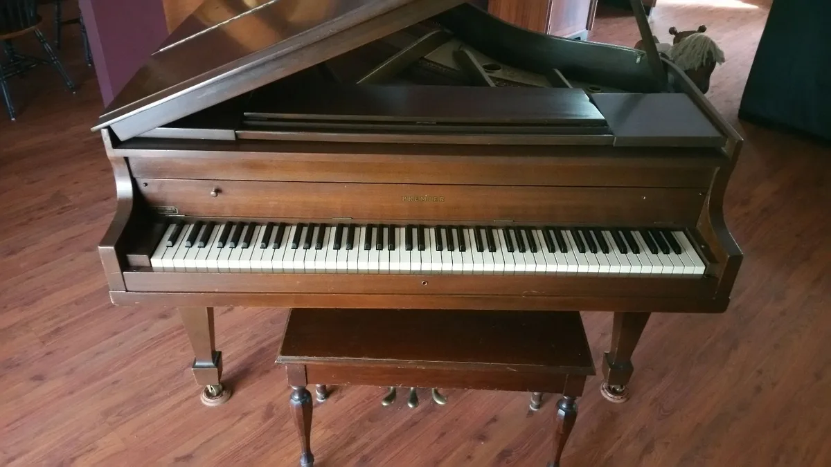 Wooden baby grand piano with bench on a wood floor